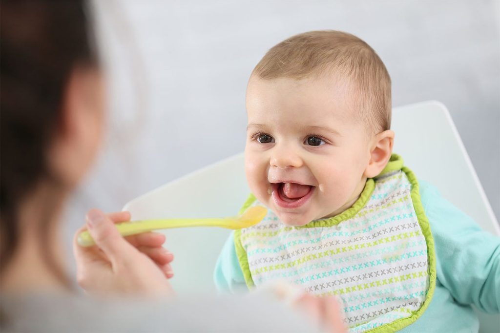 A parent feeding a baby some baby food.