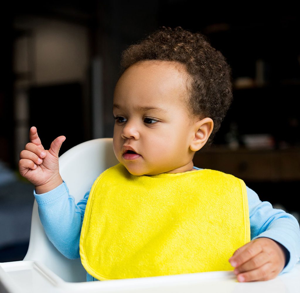 A young child wearing a bib sitting in a high chair.