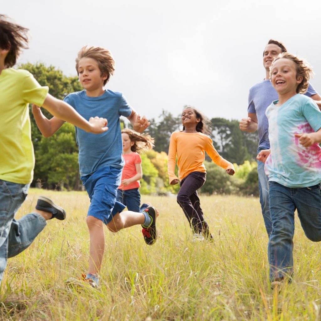 Group of kids running in a park with a dad