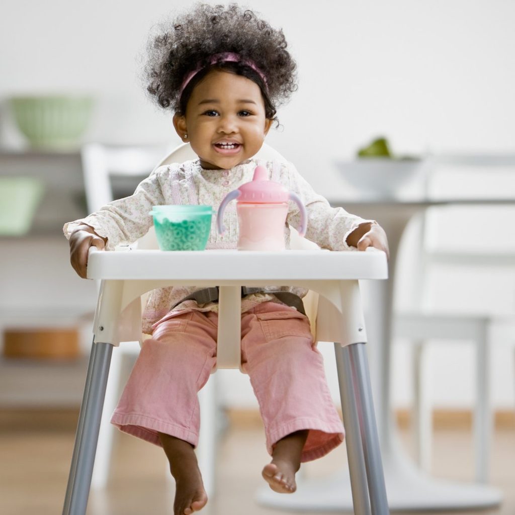 Baby in highchair with milk and cereal.