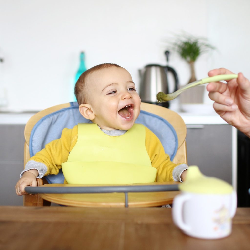 Happy baby in high chair eating