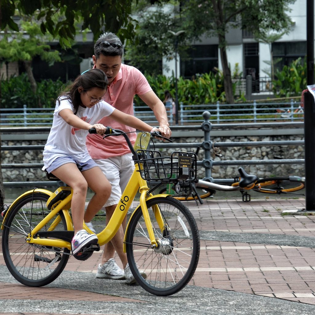 father teaching daughter to ride a bike in a park
