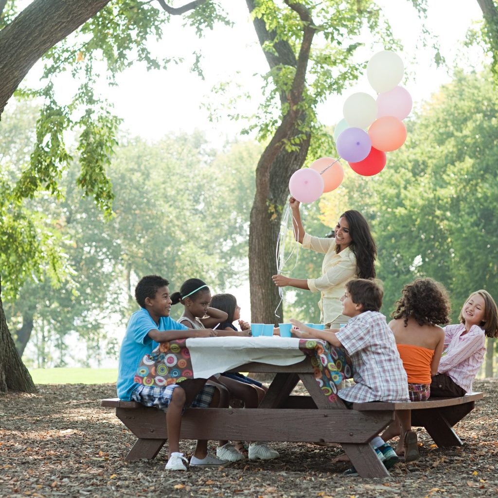 Young kids sitting at an outdoor table for a party with balloons