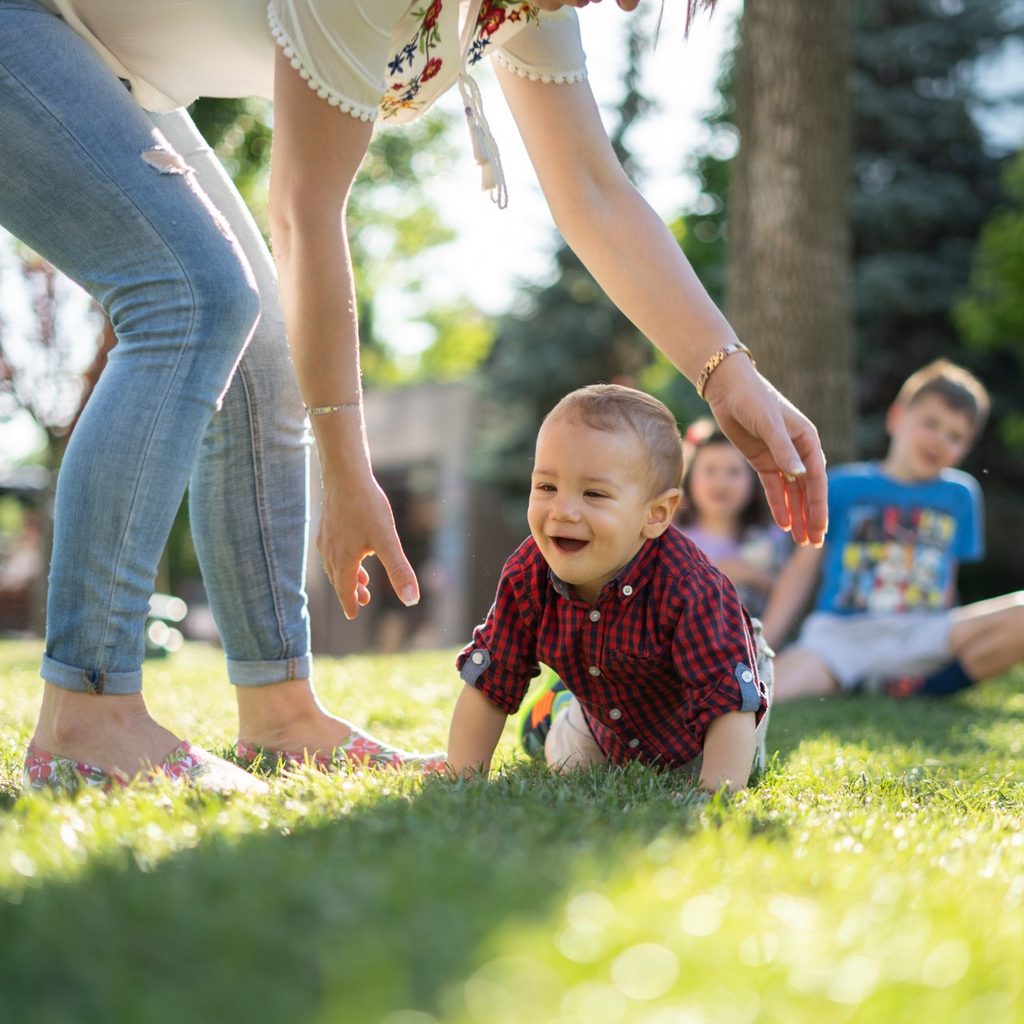 Toddler crawls on grass in park with mother watching