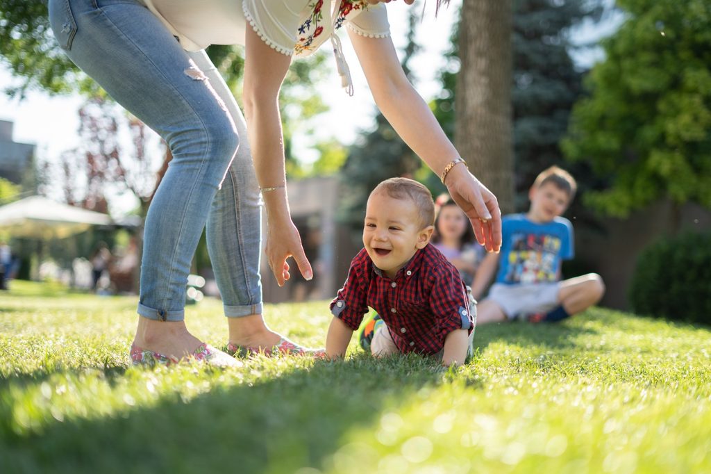 Toddler crawls on grass in park with mother watching
