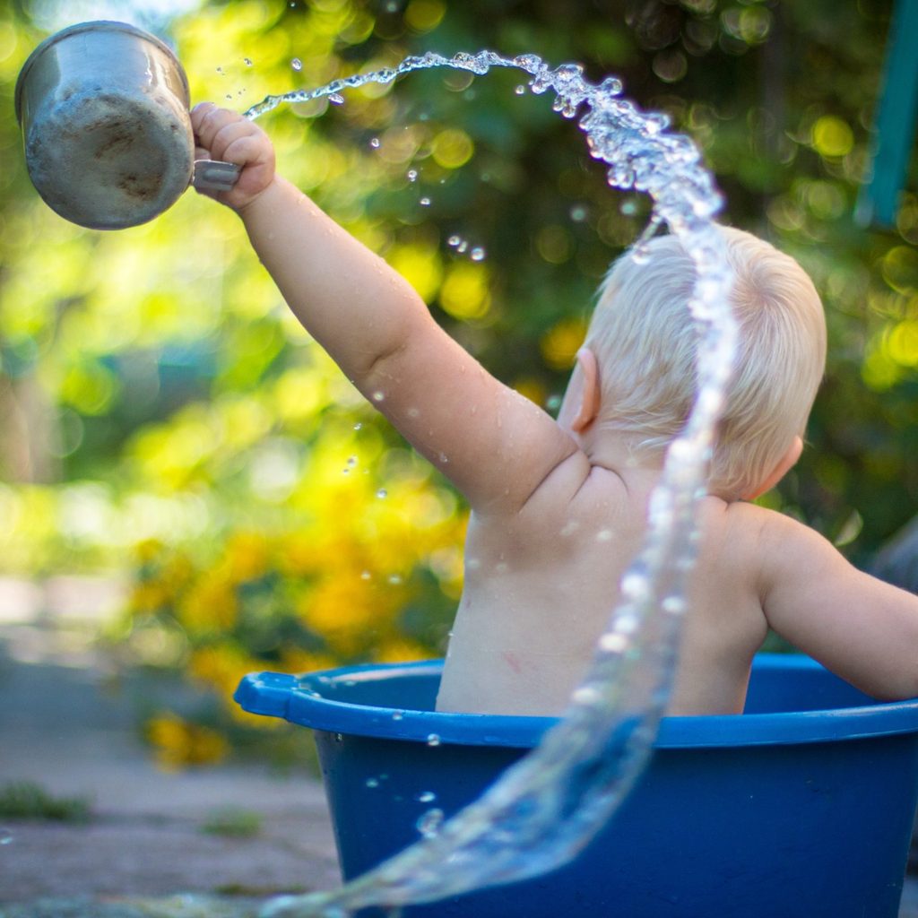 Toddler in big plastic bucket splashing water