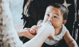 Mother feeding baby with bottle in stroller.