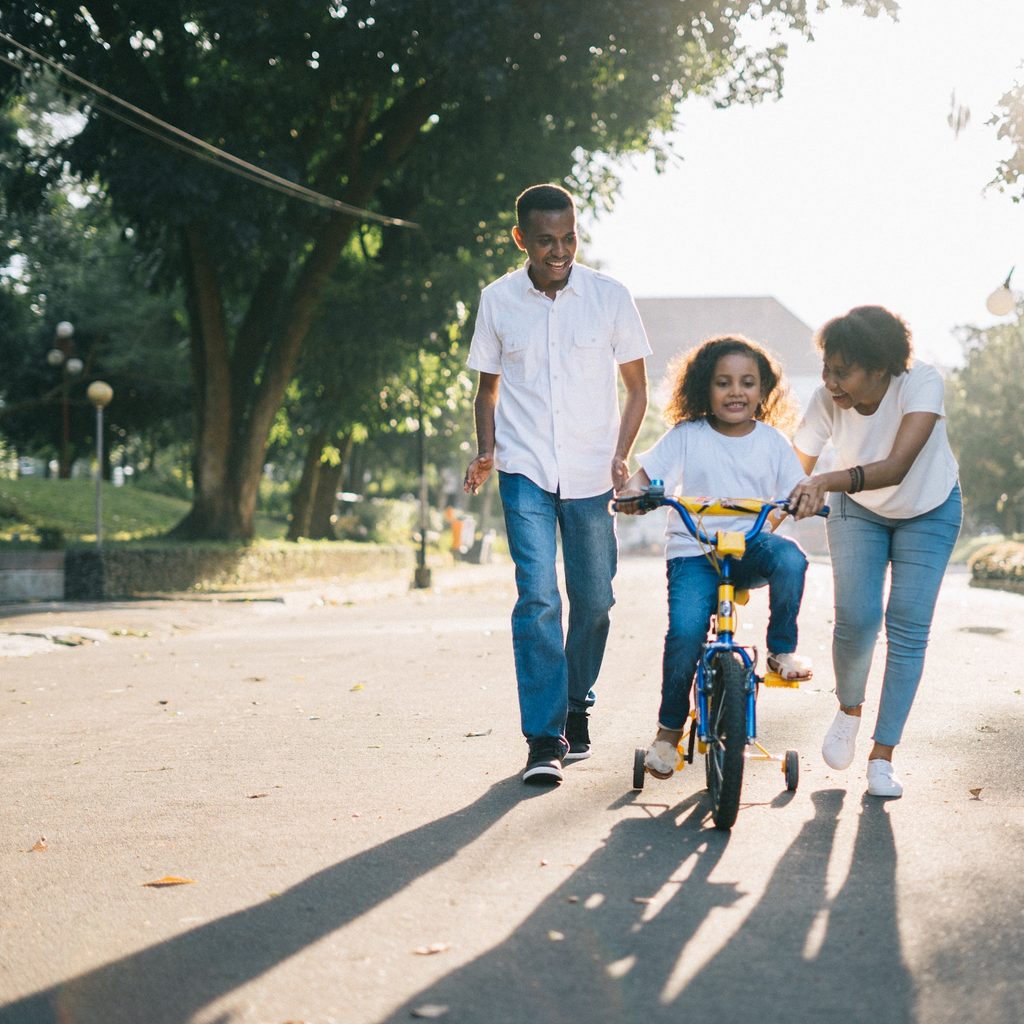 parents teaching their daughter how to ride a bike with training wheels