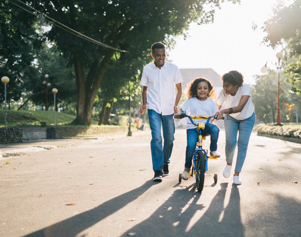 Parents teaching their daughter how to ride a bike with training wheels.