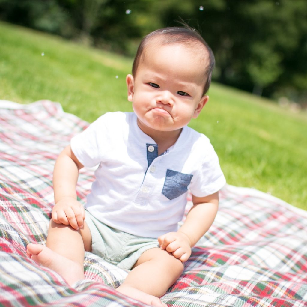 Pouting toddler on blanket in park