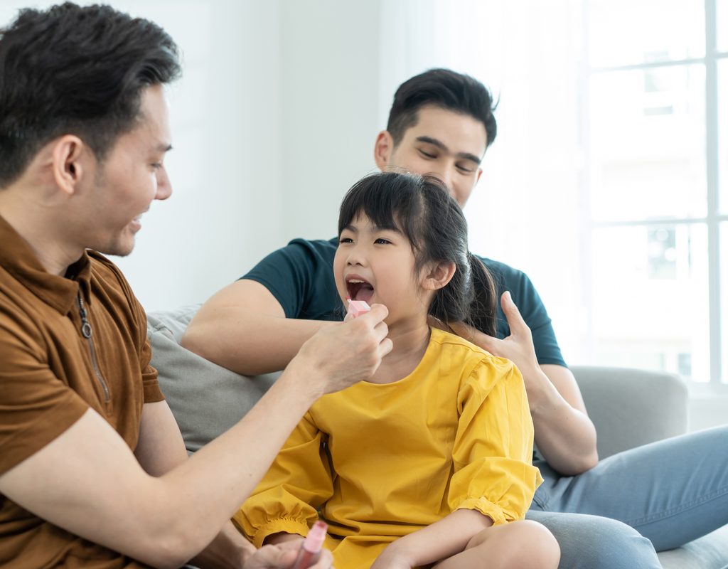 A father applying makeup to his young daughter.