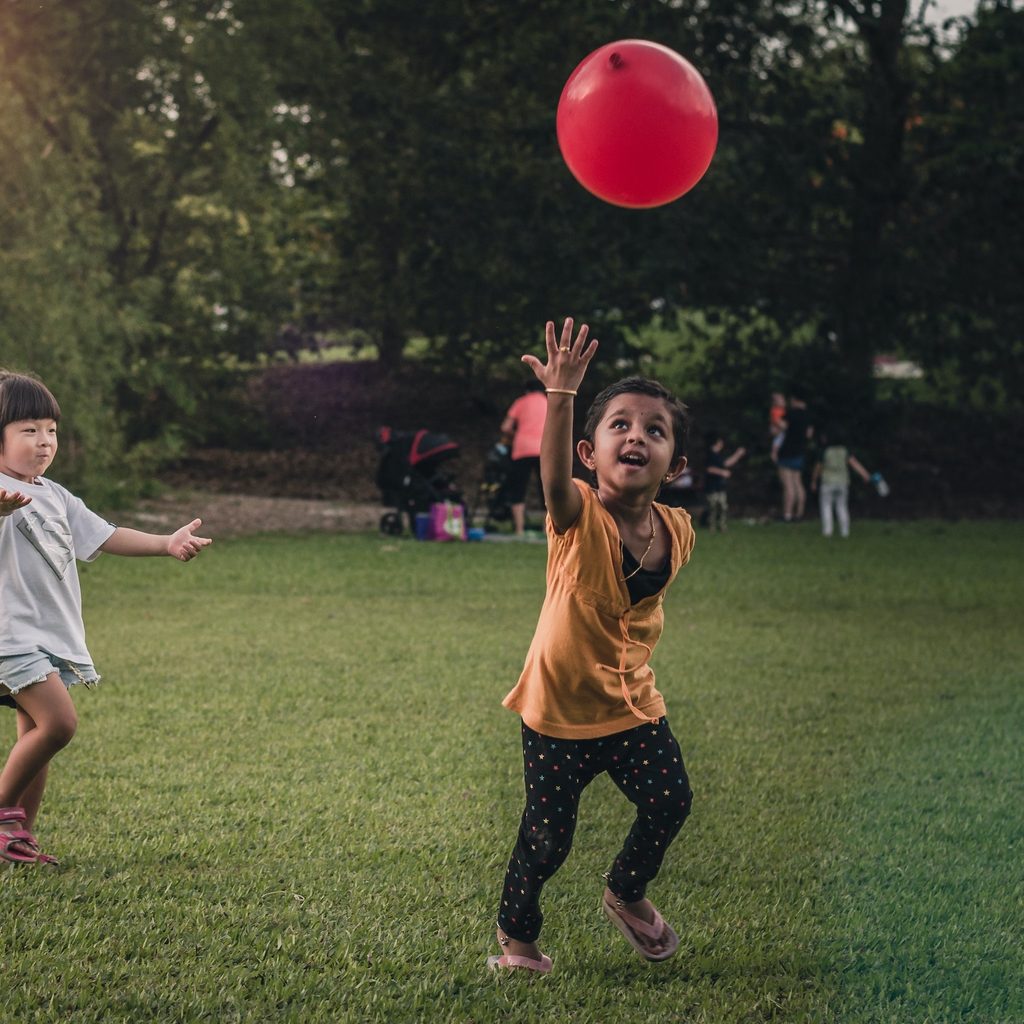 two children playing outside with a red balloon