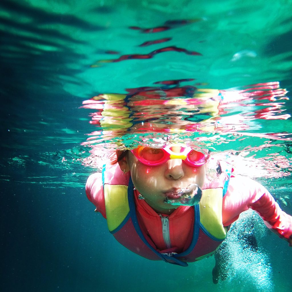Underwater photo of child wearing goggles and a vest.
