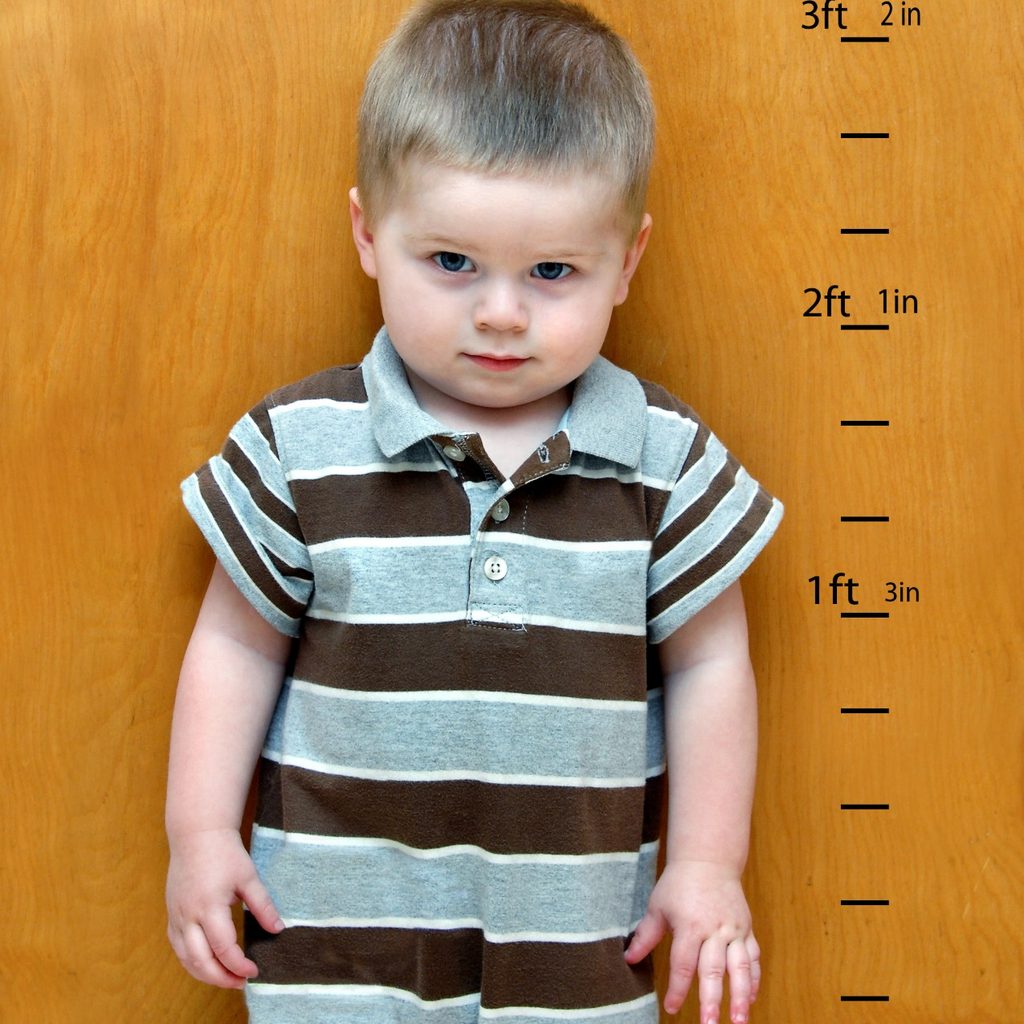 Toddler standing against a growth chart on wall.