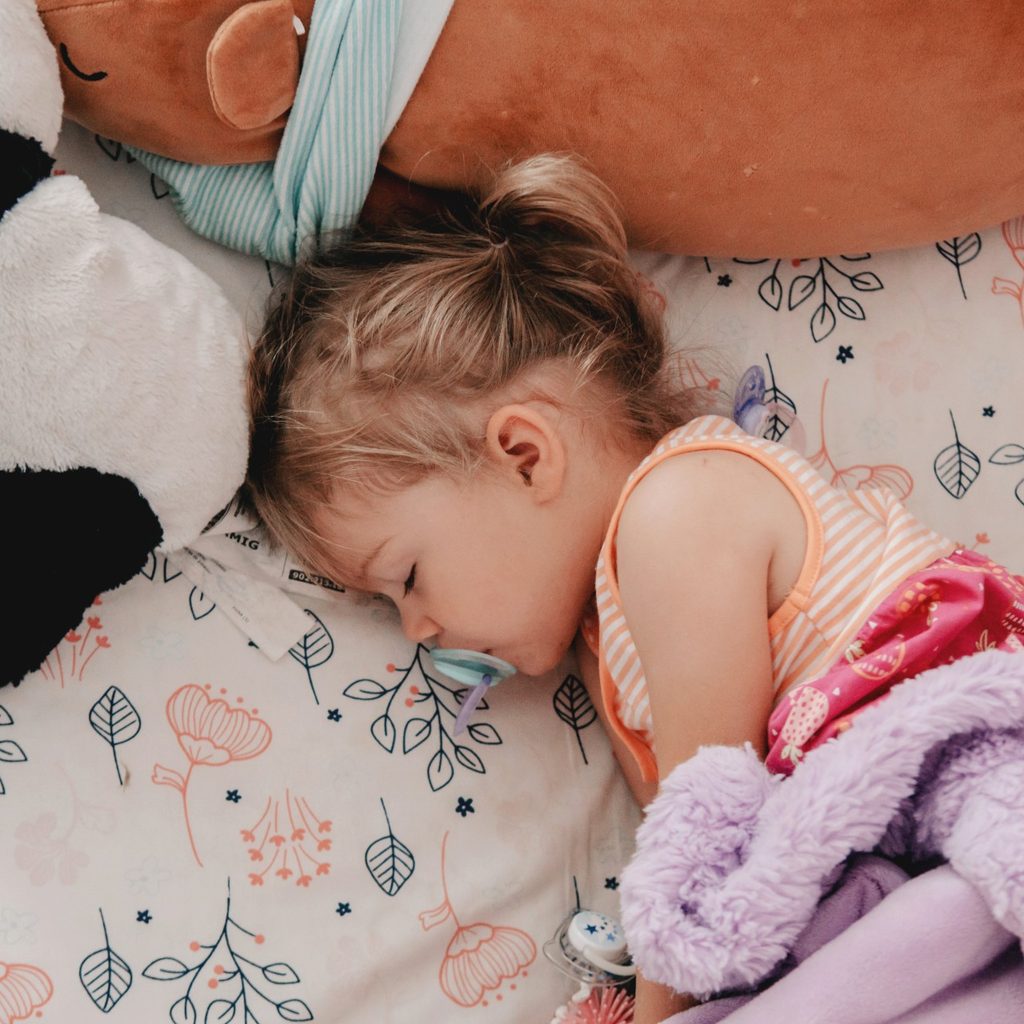 Girl toddler with pacifier napping in crib