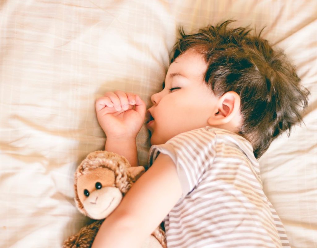 Toddler sleeping in his crib with their stuffed animal.