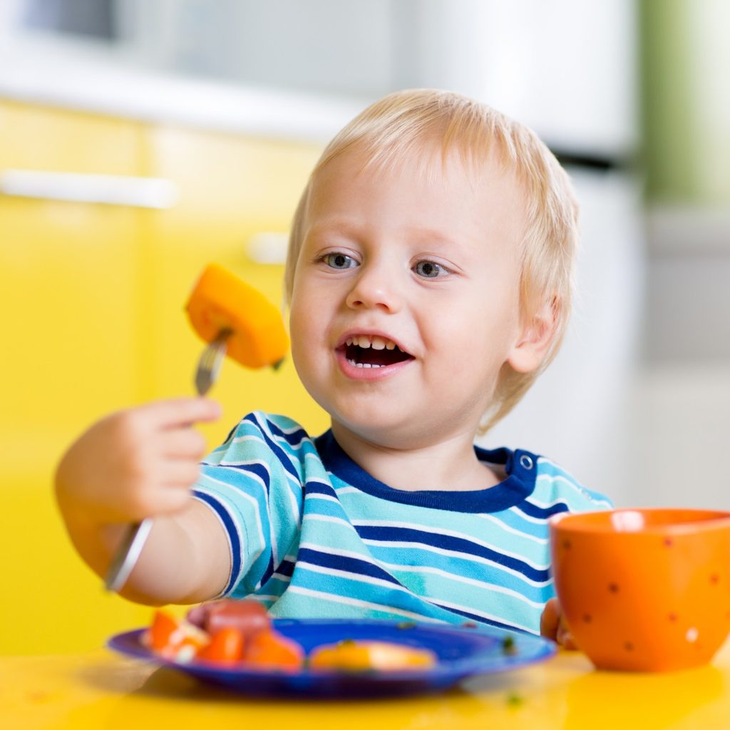 Smiling toddler at the table eating.
