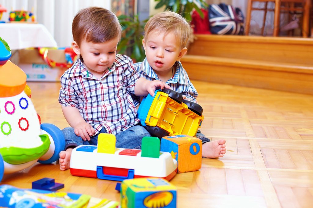 Two toddlers playing with toys on the floor