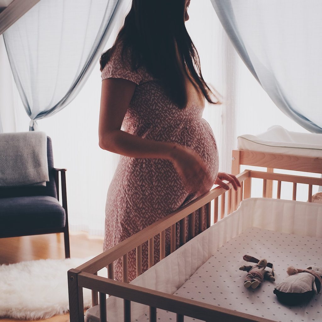 Pregnant woman standing over wooden crib in rustic nursery