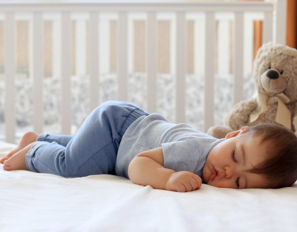 Baby sleeping in their crib with a stuffed bear.