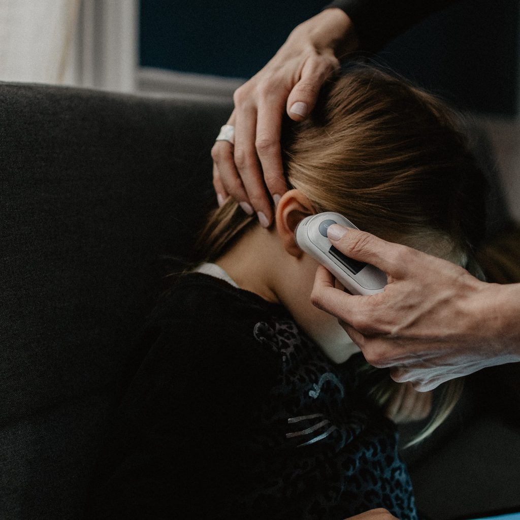 Adult taking temperature of child with thermometer in ear