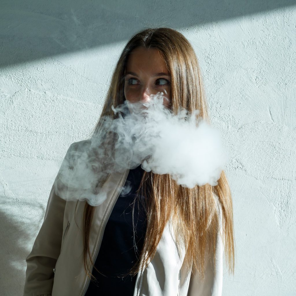Teen girl vaping near a blue wall