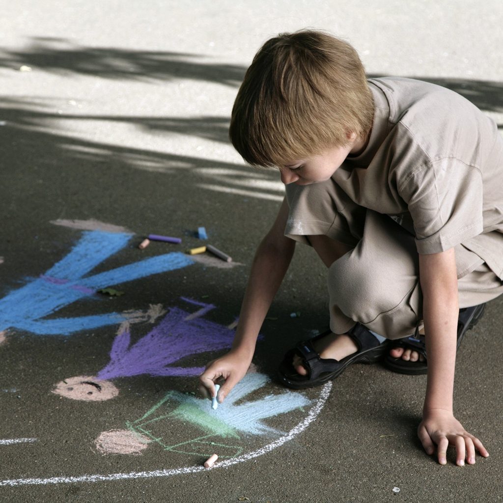 Young boy drawing with chalk on sidewalk