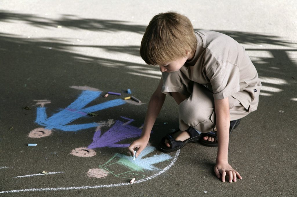 Young boy drawing with chalk on sidewalk