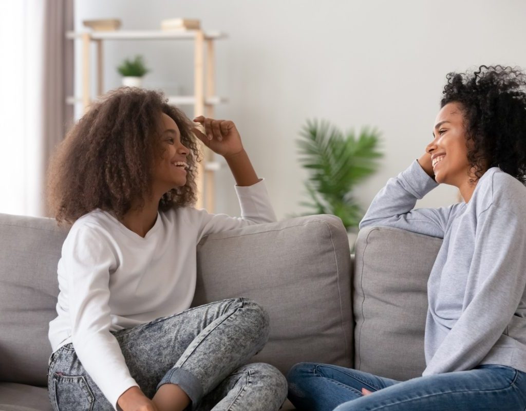 Mother and teenage daughter on couch talking.
