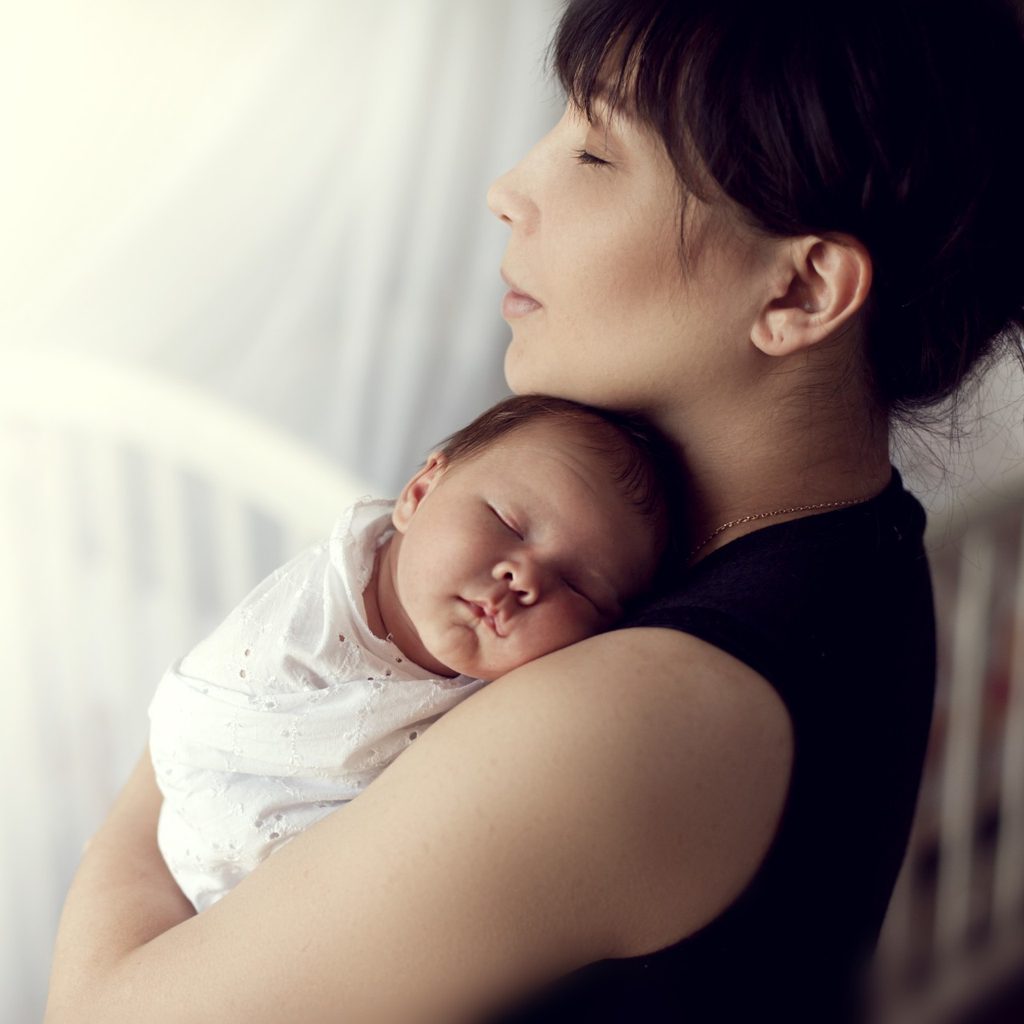 Mother holding a sleeping baby near a crib