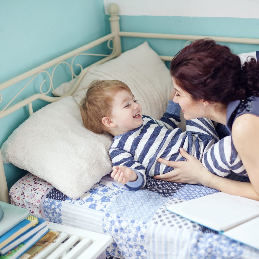 Mother laughing with toddler so in his bed