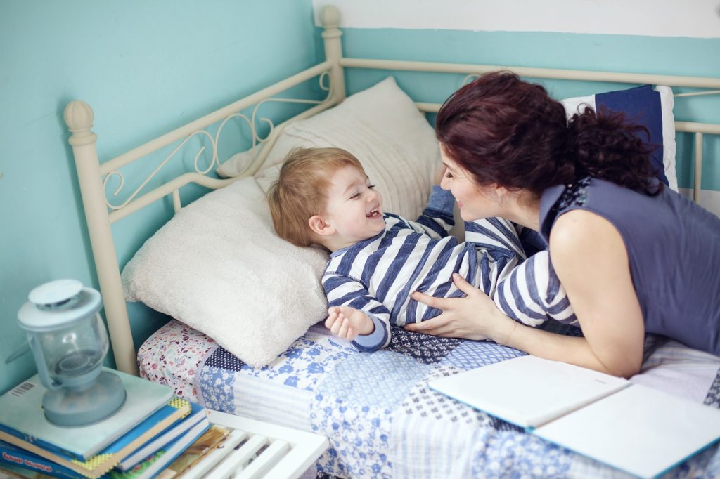 Mother laughing with toddler so in his bed