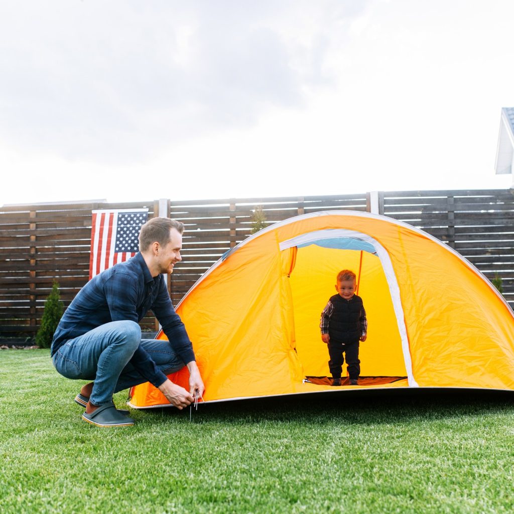 Man setting up a tent for toddler son in backyard