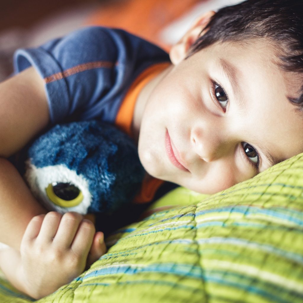 Young boy lying in bed with Teddy bear