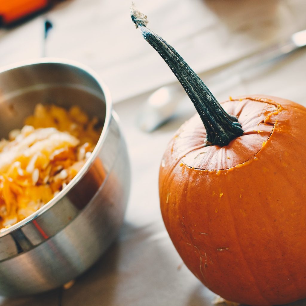 pumpkin with top carved and seeds in bowl next to it