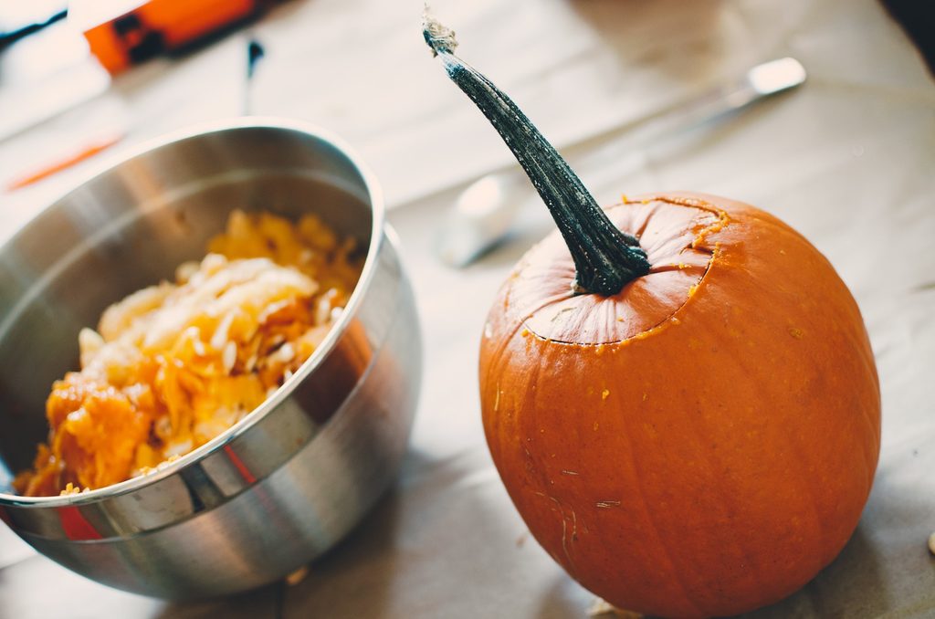 pumpkin with top carved and seeds in bowl next to it