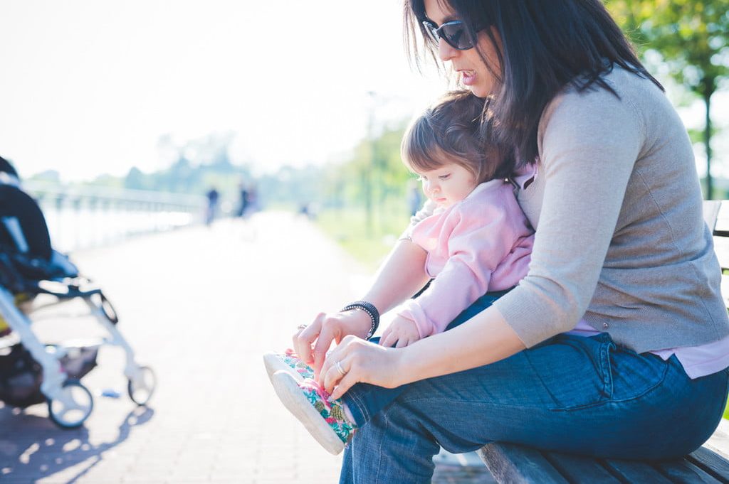 Mom tying a toddler girl's shoes as she sits on her lap