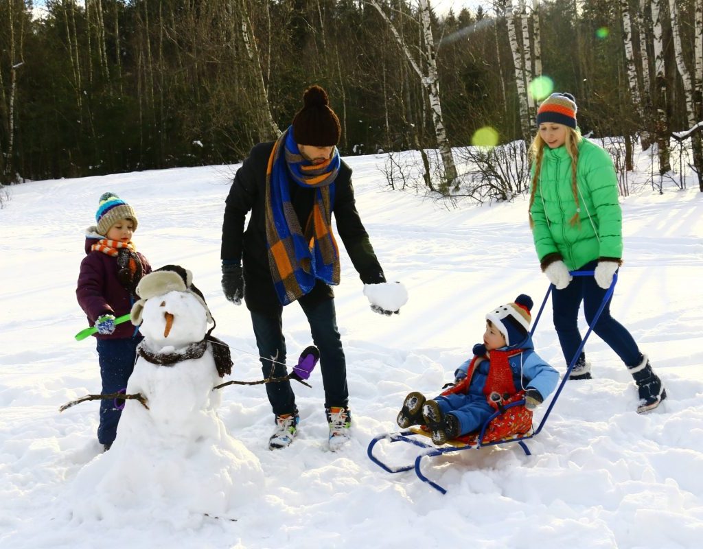 A family playing in the snow and building a snowman