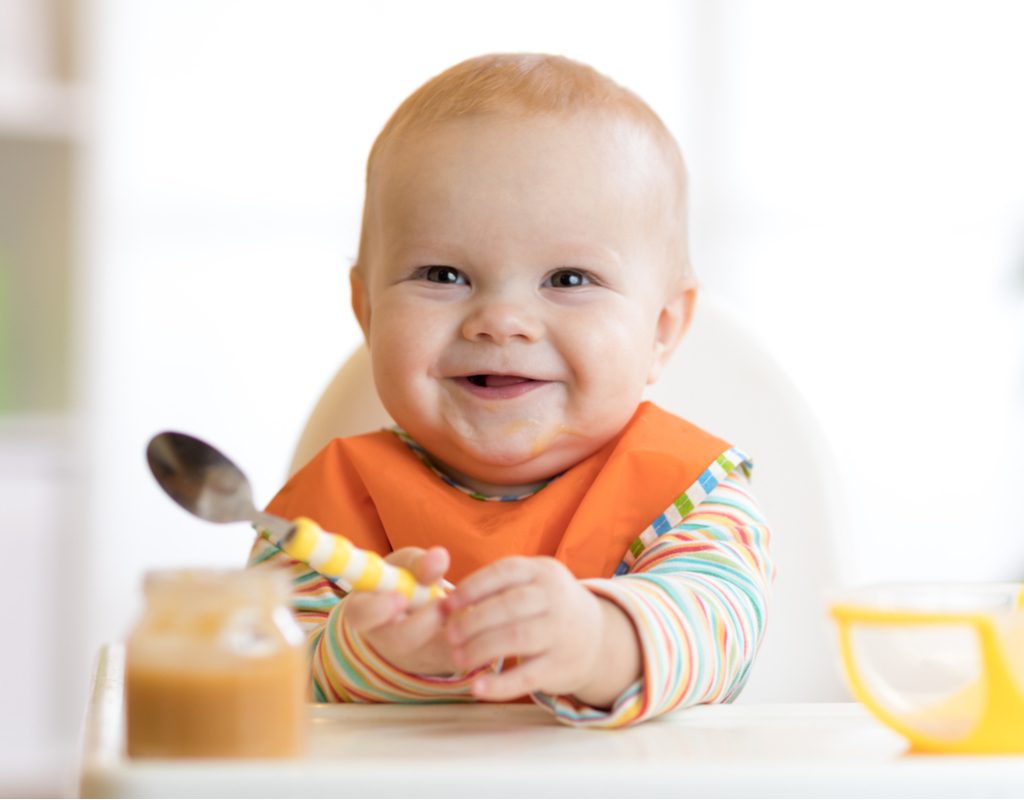 Smiling baby sits in high chair with a spoon