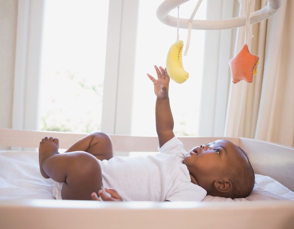 A baby playing with the mobile above their crib