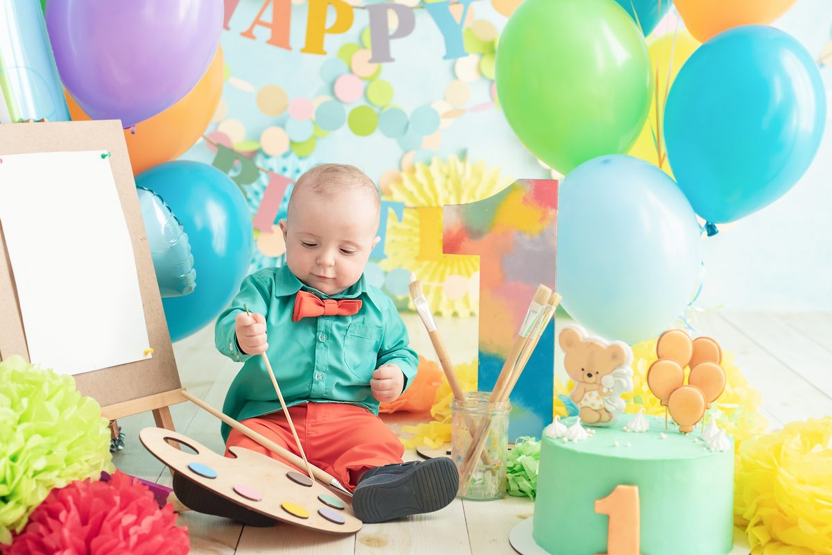 Baby boy painting with balloons and cake for his first birthday