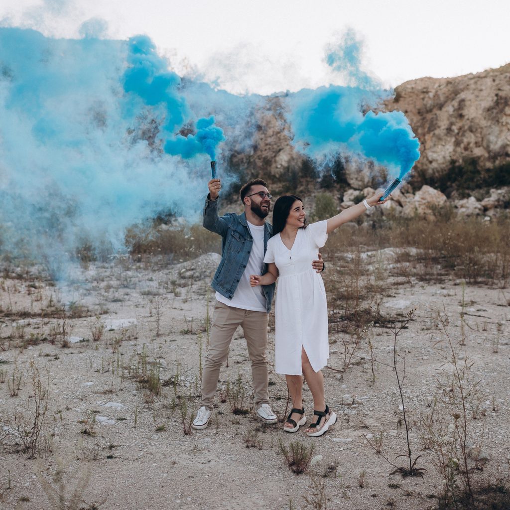 Pregnant couple holding blue smoke cannons celebrating