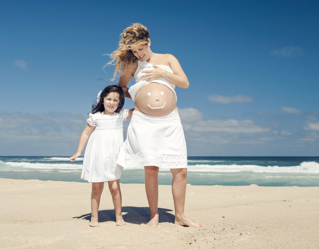 A mother and daughter wear sunscreen at the beach.
