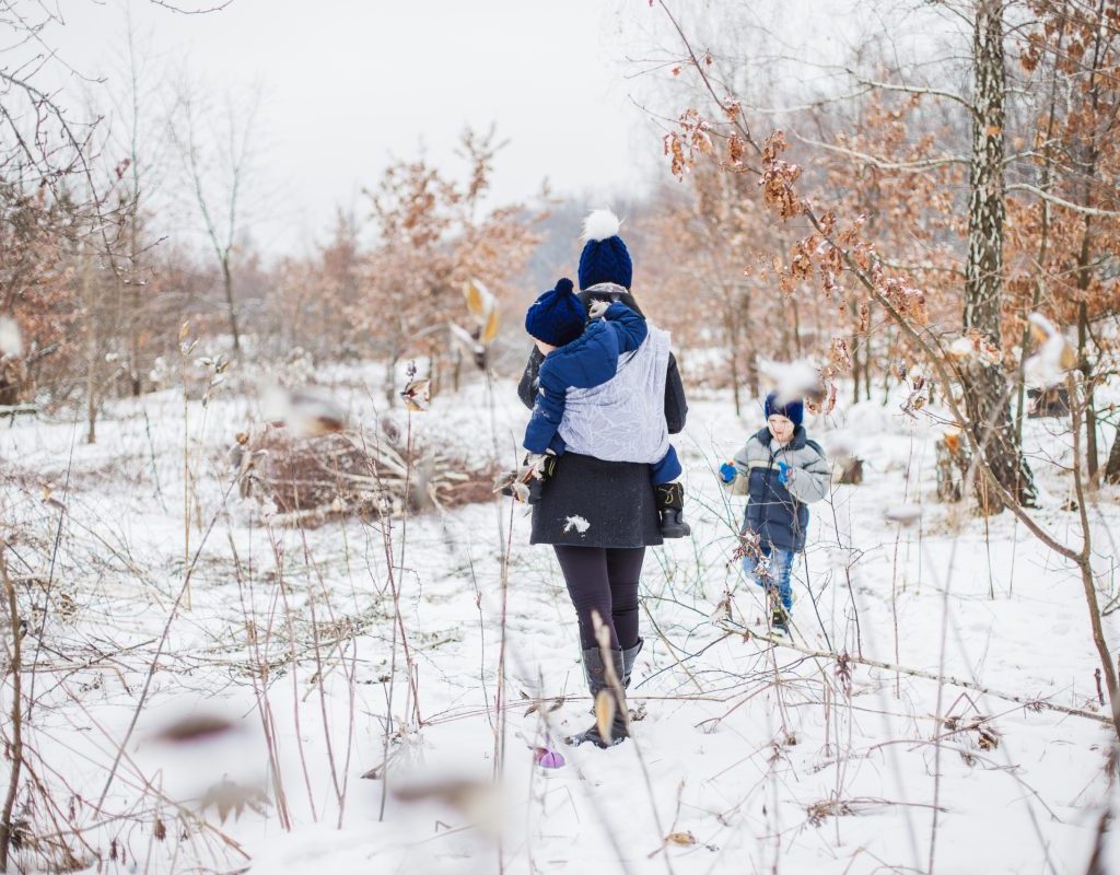 A parent walking with their two children in the snow all bundled up