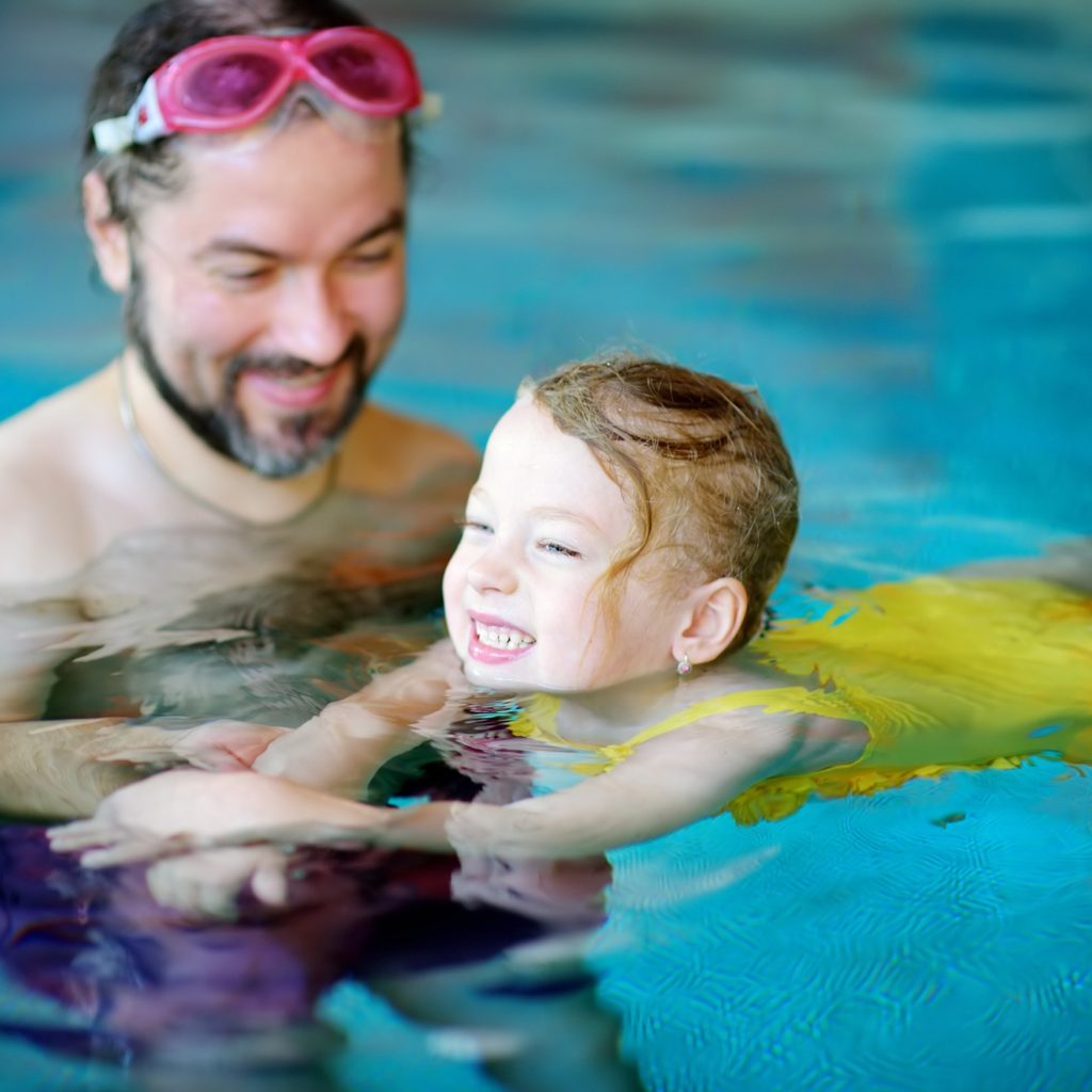 Adult teaching child to swim in a pool.