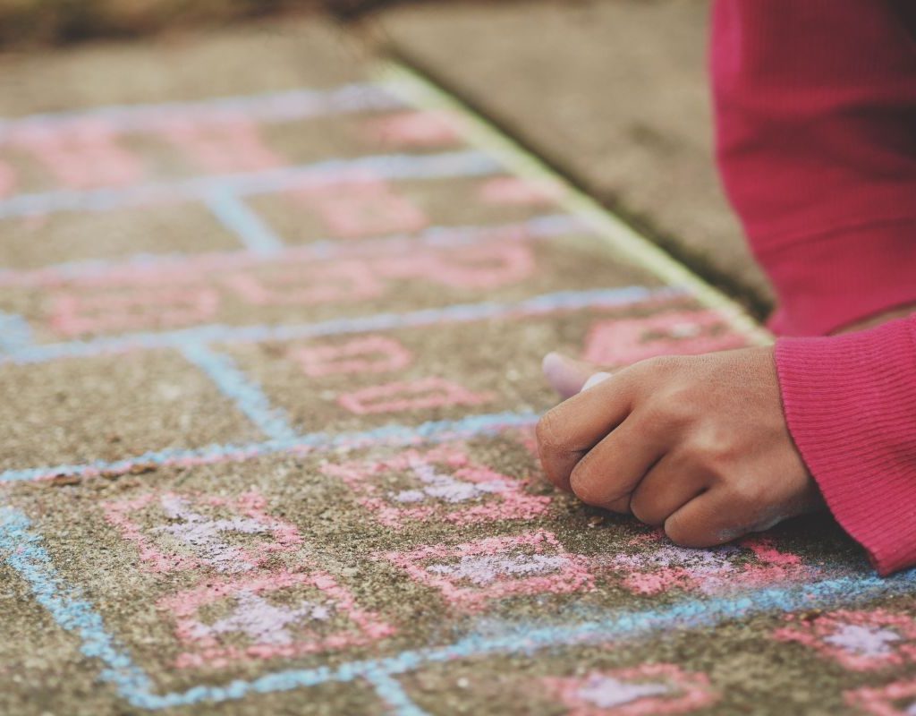 A girl drawing hopscotch with chalk on a sidewalk