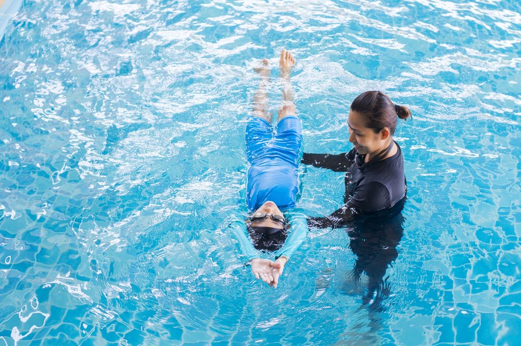 Trainer teaching a young student to swim in a pool.