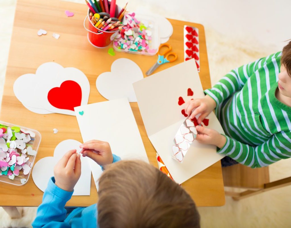 two boys make Valentine's cards at a table full of paper, hearts, and art supplies