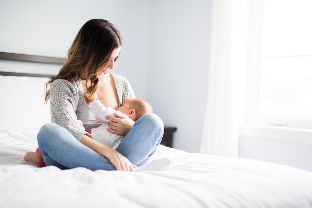 Mom breastfeeding baby on bed.