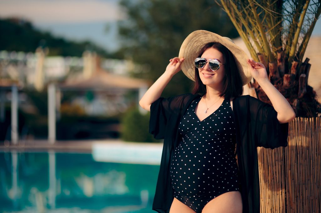 Pregnant woman in a bathing suit by a pool enjoying the sun